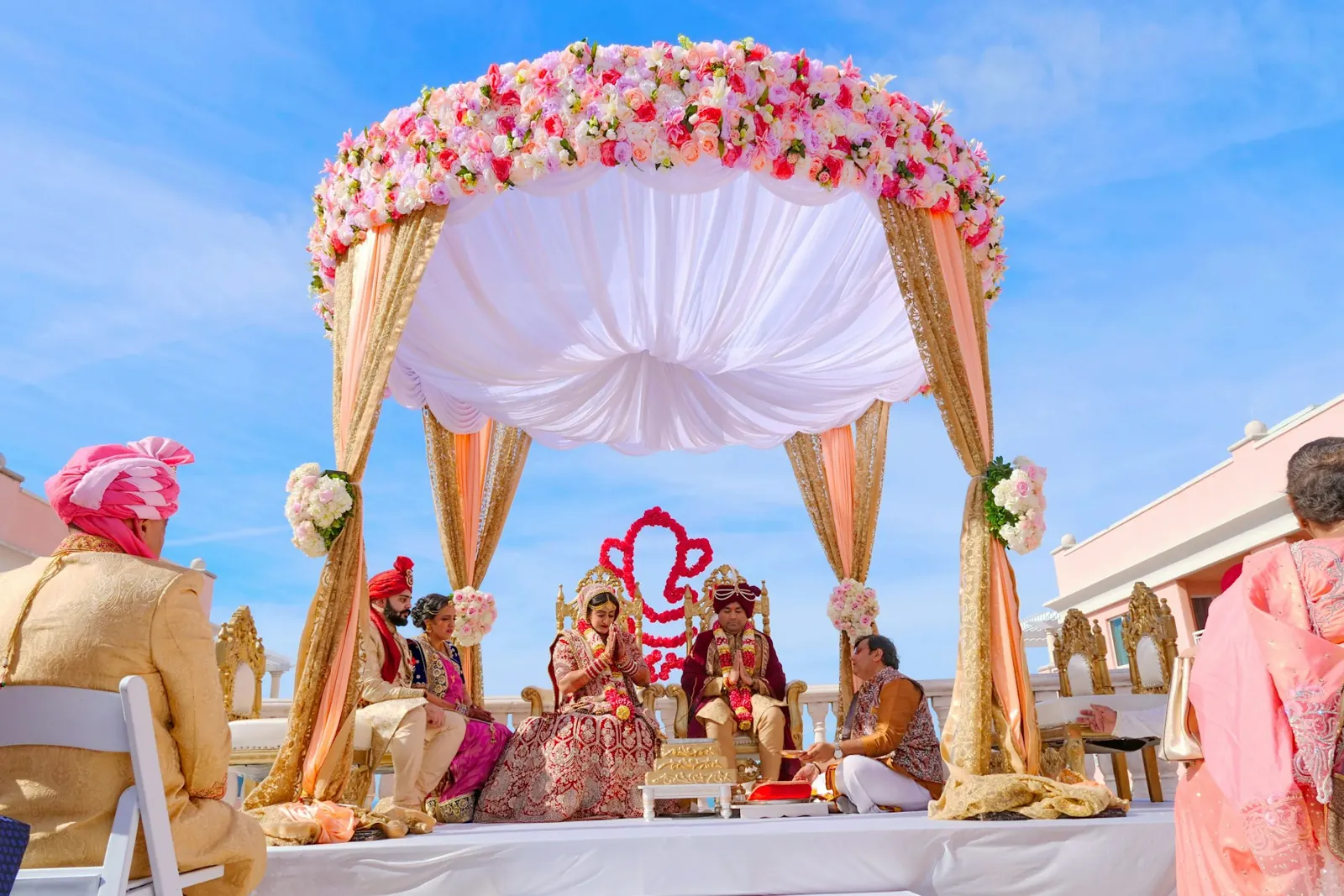Couple seated under a floral mandap during an outdoor wedding ceremony